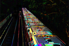 Fotografie von Hilmar Sundermann in surrealer Bearbeitung. U-Bahn und Gleise von oben neben dichtem Bewuchs. Zug und Gleise führen vielfarbig schillernd zum dunklen, teilweise schwarzen Hintergrund.
