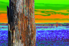 Fotografie von Hilmar Sundermann in surrealer Bearbeitung mit kräftigen Farben. Im Vordergraund ein verwitterter Holzpfahl vor einem Gewässer mit roter Backbordtonne im Hintergrund; darüber ein stark verfärbter Himmel.
