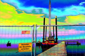 Fotografie von Hilmar Sundermann in surrealer Bearbeitung mit kräftigen Blau- und Gelbtönen. Blick durch einen Bauzaun mit gelbem Schild „Betreten der Baustelle verboten“ entlang dem Holzsteg der alten Seebrücke zum Schwimmponton mit vier Stelzen, darauf ein hoher Kran vor stark verfärbtem leuchtendem Himmel.