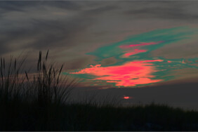 Fotografie von Hilmar Sundermann in surrealer Bearbeitung mit kräftigem Rotorange, Grün und Grau. Sonnenuntergang über Dünen mit Gras an der Ostseeküste bei Ahrenshoop.