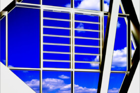 Fotografie von Hilmar Sundermann in surrealer Bearbeitung. Großes, geometrisch gegliedertes Fenster mit Blick auf blauen Himmel und Wolken, davor steht eine Person mit verschränkten Händen und blickt aus dem Fenster.
